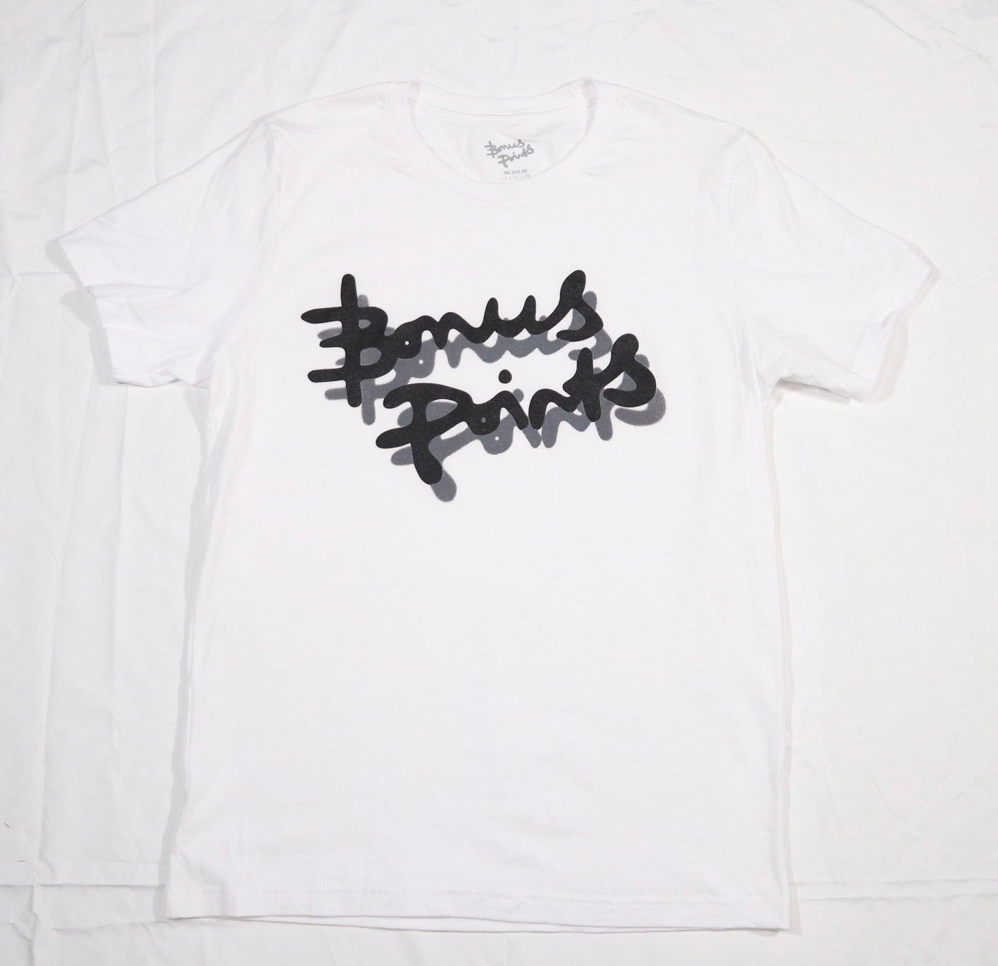Flat lay of a White T-shirt in a soft fabric, displayed on a clean white background. The T-shirt features the Bonus Points Logo across the chest in Black ink, with a gray drop shadow.