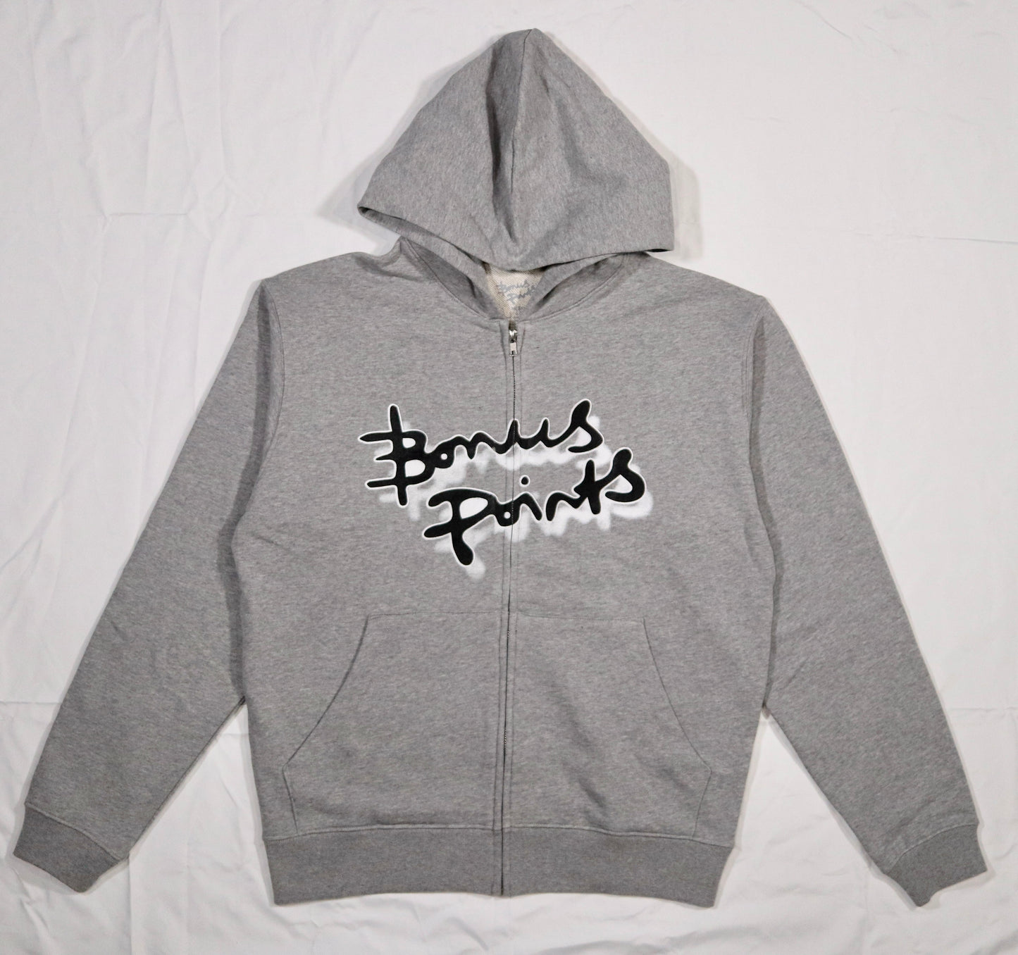 Flat lay of a Gray Zip-up hoodie in a soft fabric, displayed on a clean white background. The hoodie features the Bonus Points Logo across the chest in black ink, with a white stroke outline, and a white drop shadow. Hoodie has two front pockets and chrome zipper.