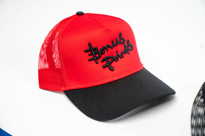 Side View of Red and Black “Extra Credit” Trucker. Black Brim with Red Upper and Bonus points logo in black puff embroidery across front panel.